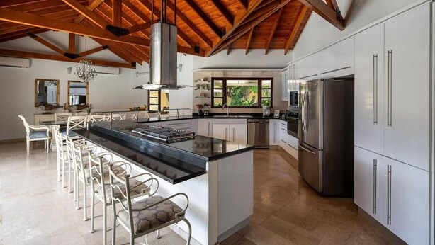 Una cocina amplia con una isla central, armarios blancos, electrodomésticos de acero inoxidable y un alto techo de madera.