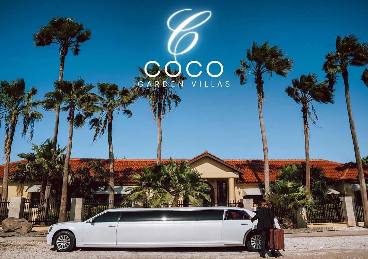 A white limousine parked in front of a house with a red-tiled roof and palm trees.