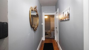 A hallway with a black carpet, a gold-framed mirror, and a cityscape picture on the wall. - Remodeled, Spacious, Furnished - Brady St Apartment for Monthly Rental (Milwaukee)