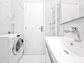 A modern bathroom with a washing machine, a sink with a mirror, and a door. - Athens Divas One Paradise (Athens)