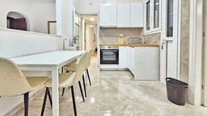 Une cuisine moderne avec des meubles blancs, un four encastré et un coin repas comprenant une table et des chaises blanches.
