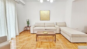 Un salon moderne avec un parquet en chevrons, un canapé d’angle beige, une petite table basse en bois et une plante en pot.