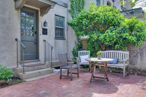 A brick patio with a wooden bench and chairs, a small table, and a door with a window. - Shared Hot Tub: Historic Cottage, Walk to Elm Park (Worcester)