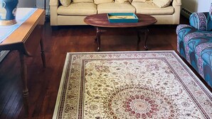 A living room with a beige sofa, a wooden coffee table, a patterned rug, a ceiling fan, and decorative wall art.
