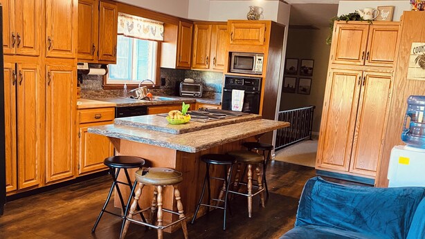 A compact kitchen with wooden cabinets, a central island with stools, a microwave, a toaster, and a water dispenser.
