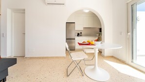 A modern kitchen with white cabinetry, a dining area with a white table and chairs, and a large window providing natural light. - CT 288 AL   Faro's Retamar Cuddly Nest for 2 (Almería)