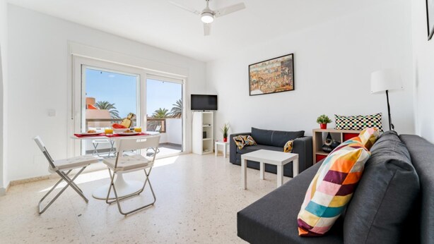 A modern living room with a grey sofa, a small white table, and a dining area with a white table and chairs. - CT 288 AL   Faro's Retamar Cuddly Nest for 2 (Almería)