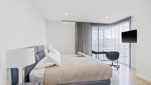 Et moderne hotelværelse med seng, skrivebord, stol, fjernsyn og et vindue med gardiner.