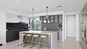 Una cocina moderna con una isla central, taburetes de bar, iluminación colgante y vistas al exterior.