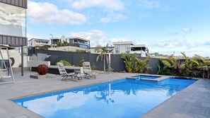 En moderne udendørs swimmingpool med liggestole og en dekorativ stenskulptur.