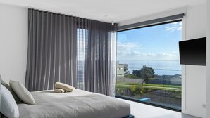 Un dormitorio moderno con un ventanal grande, una cama con almohadas y un televisor de pantalla plana.