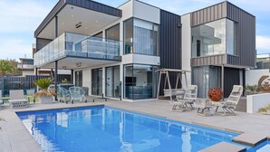 Una casa moderna de dos pisos con piscina, mobiliario exterior y una gran escultura decorativa.