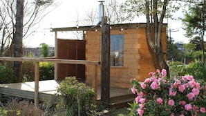 A wooden cabin with a deck, surrounded by greenery and pink flowers. - Lynwood house (Cobh)
