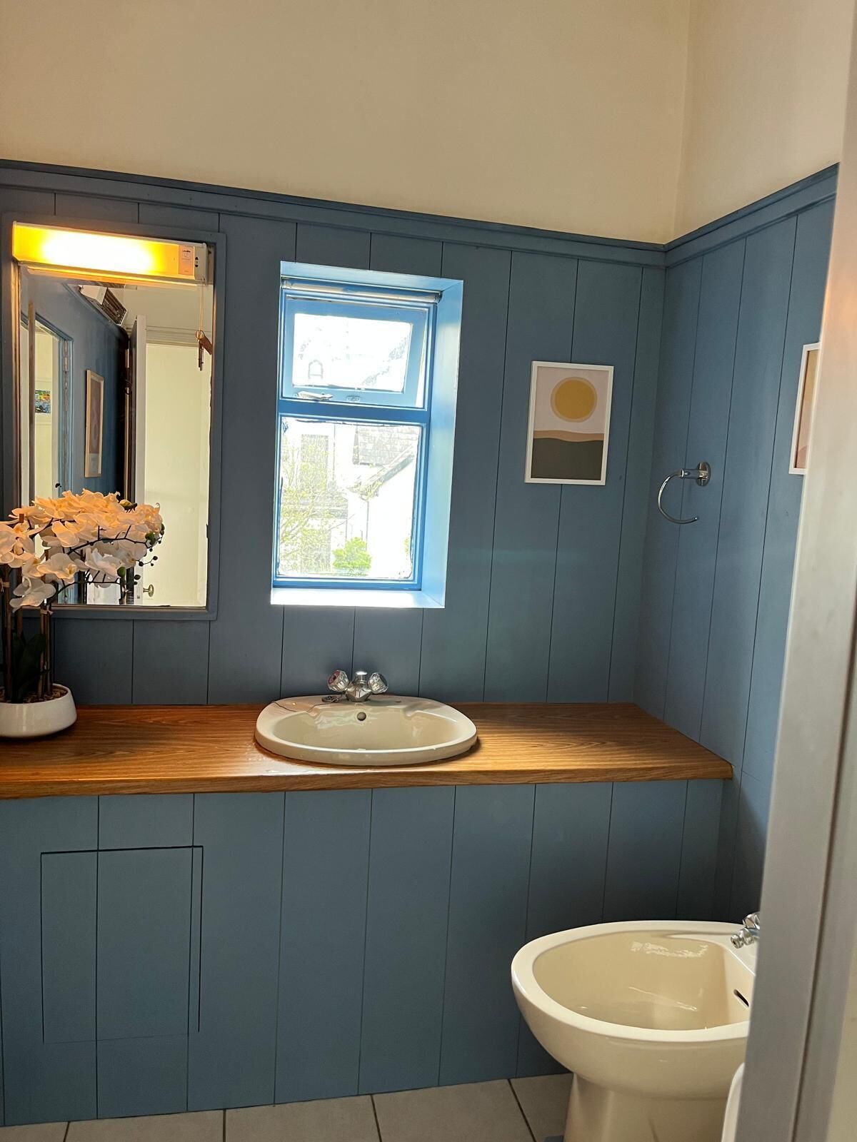 Un baño con tocador de madera, lavamanos, espejo, ventana y retrete.