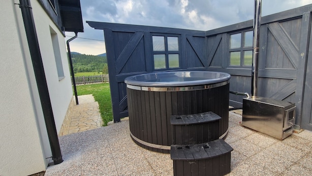 Un jacuzzi con escalones y una sauna en un patio trasero con un sendero de piedra y una valla de madera.