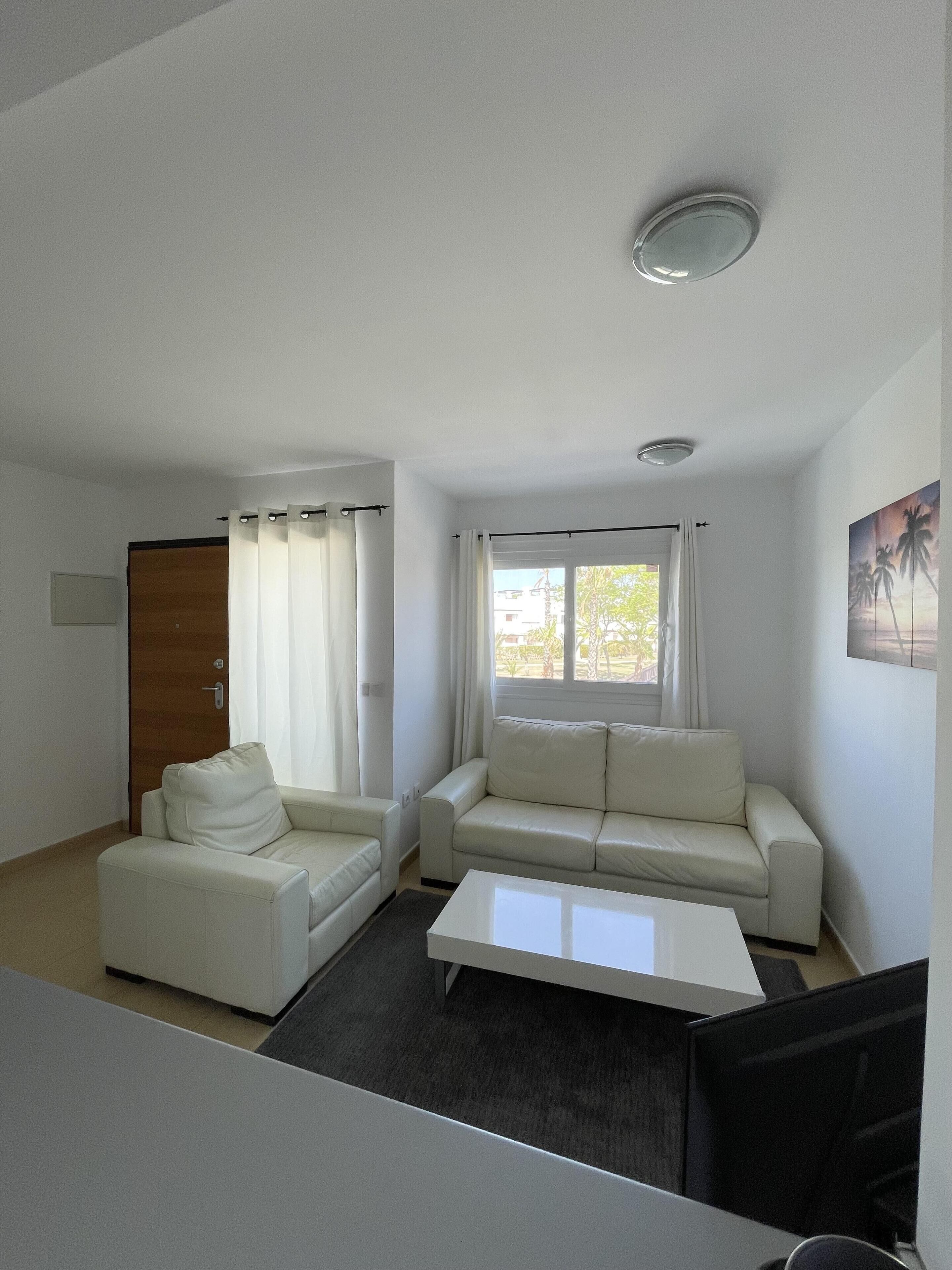 Una sala moderna con un sofá blanco, un sillón más pequeño y una mesa de centro.