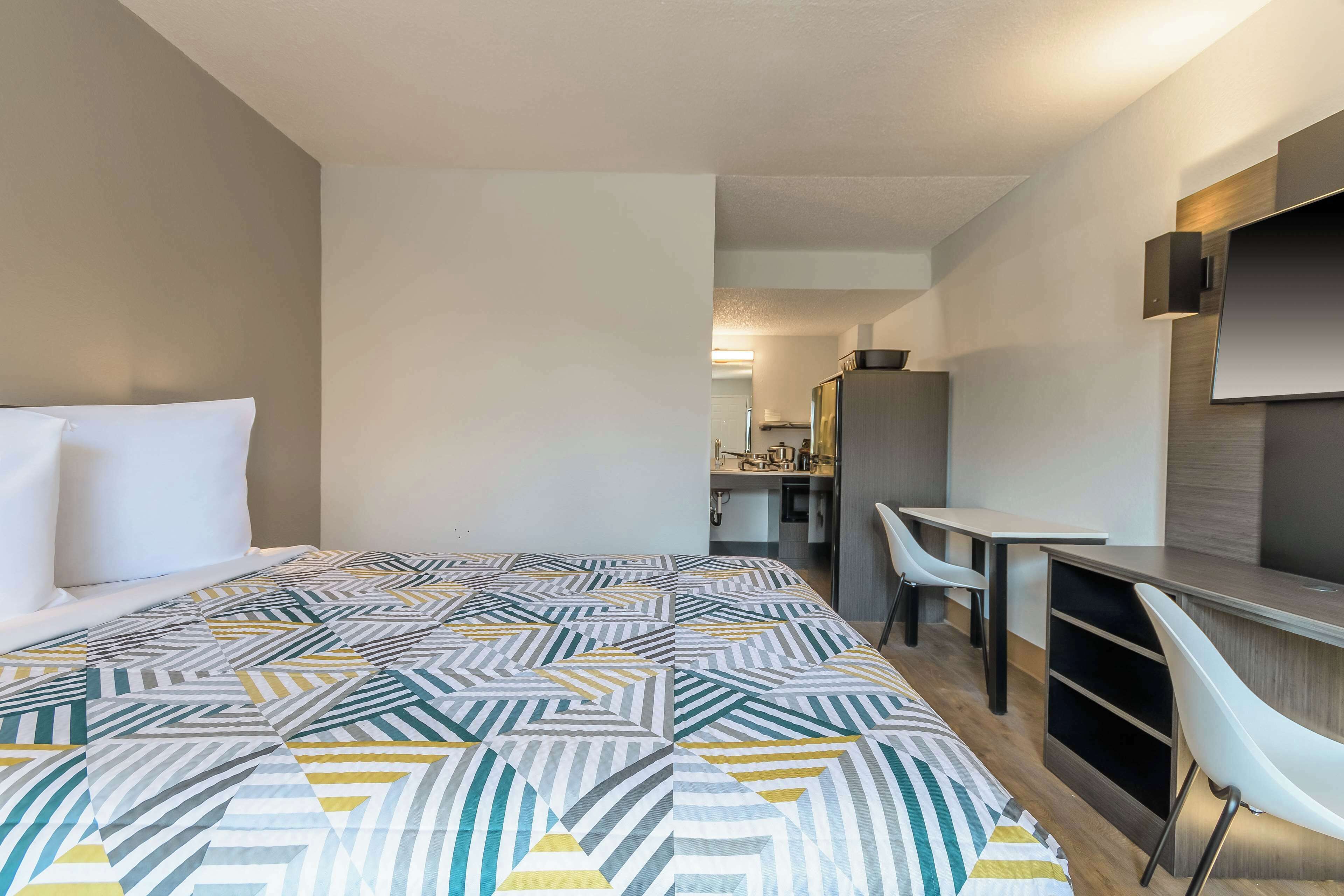 A modern hotel room with a large bed, a desk, and a TV mounted on the wall.