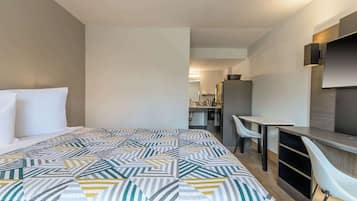 Una habitación de hotel moderna con una cama grande, un escritorio y un televisor montado en la pared.