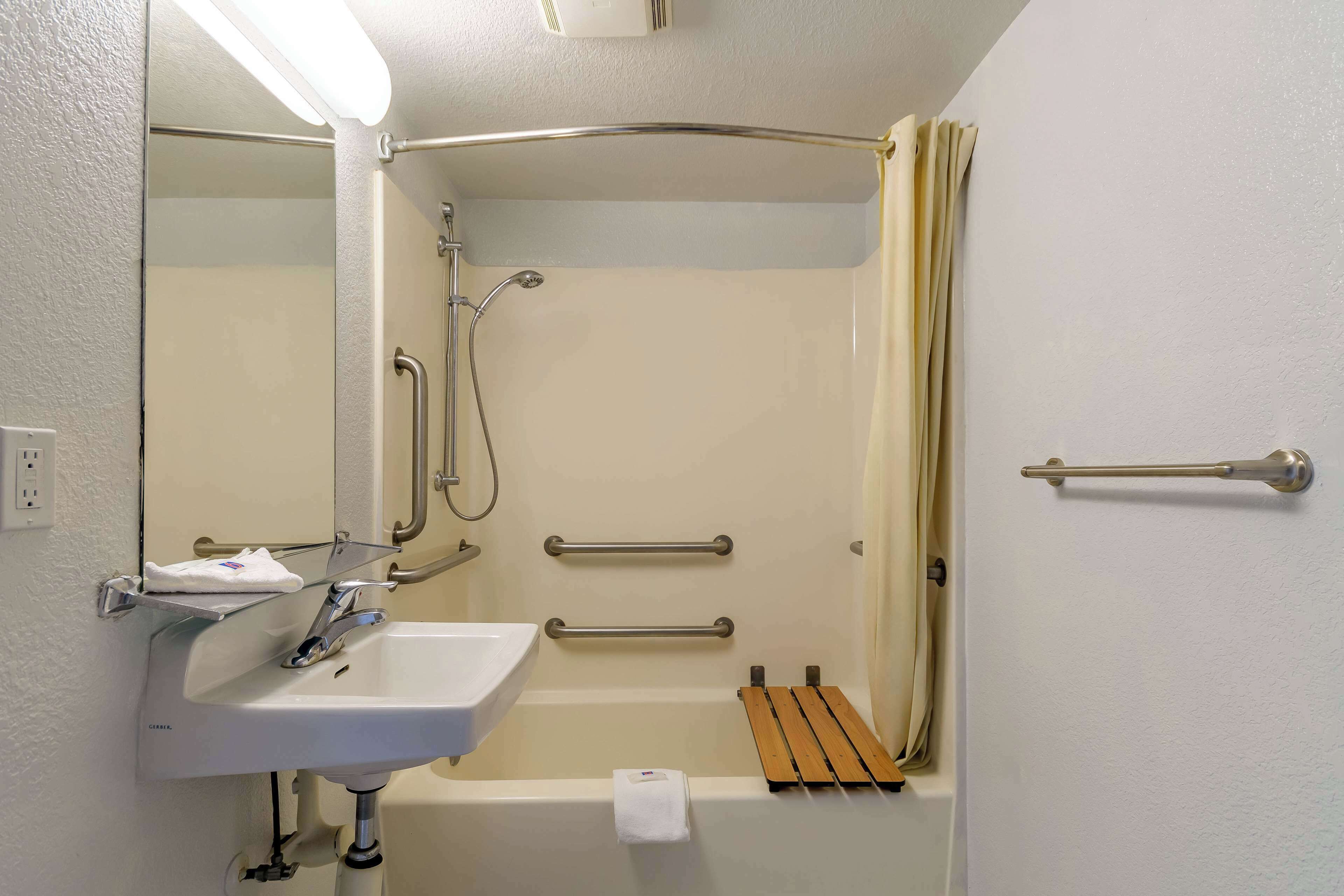 A bathroom with a white sink, a mirror, a shower with a glass door, and a wooden shelf.