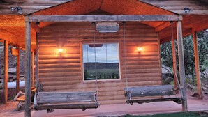 A log cabin with a porch, two swings, and a view of the landscape through a window.