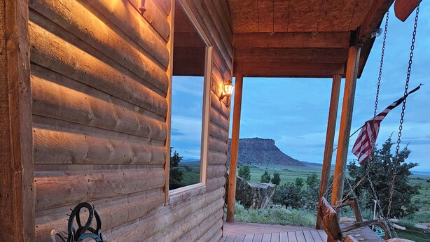 A wooden log cabin with a porch, a metal horse sculpture, and a view of a mountain.