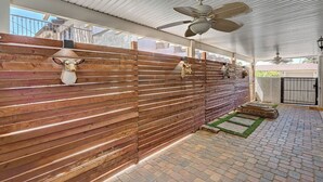 Un espace extérieur abrité, doté d’une clôture en bois, d’un ventilateur de plafond et d’une terrasse dallée.