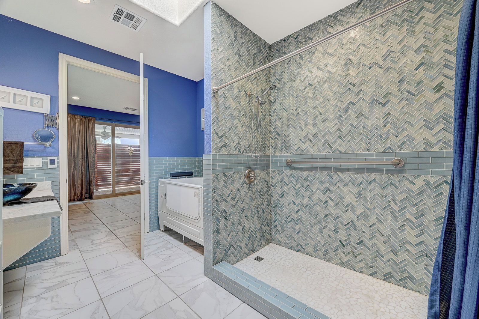 Un bagno con zona doccia rivestita in pattern a spina di pesce, un mobile lavabo bianco con specchio e una parete decorata in blu.