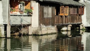 A traditional wooden house with a thatched roof, a wooden balcony, and a waterway beneath.