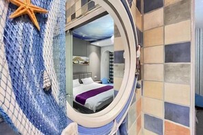 Une chambre avec un lit, une décoration en forme d’étoile de mer et une vue à travers une fenêtre circulaire.