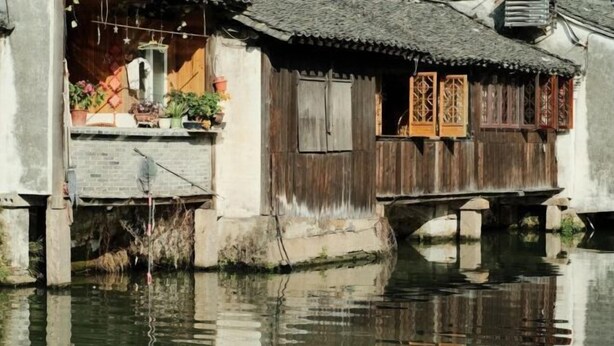Una casa de madera tradicional con tejado de tejas, construida sobre el agua, con un pequeño balcón y plantas en macetas.