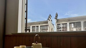 Vista de un edificio tradicional con tejado de tejas y chimenea, visible a través de una ventana con pared de paneles de madera.