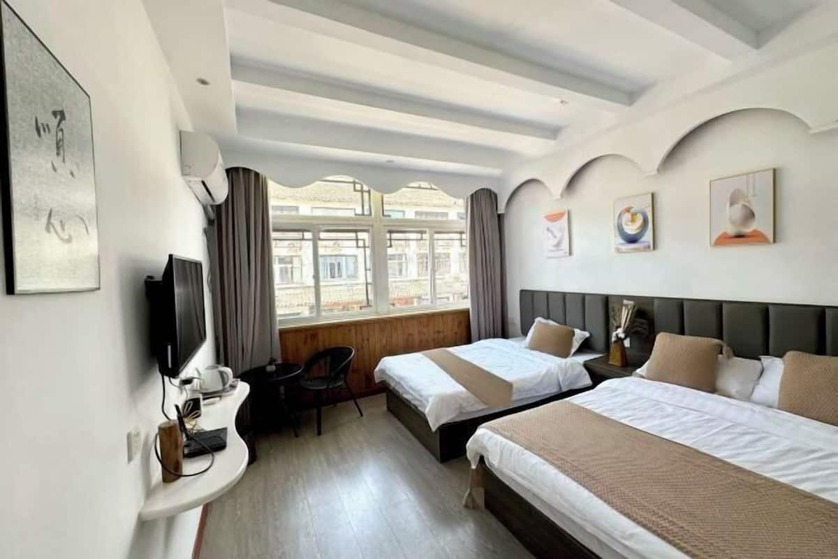 A hotel room with two beds, a desk with a computer, a TV, and a window with curtains.