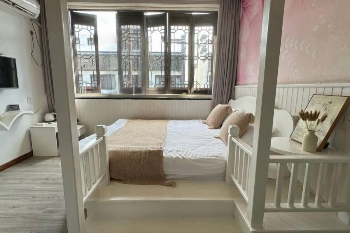 A bedroom with a four-poster bed, a window with decorative iron bars, a bedside table, and a framed picture on the wall.