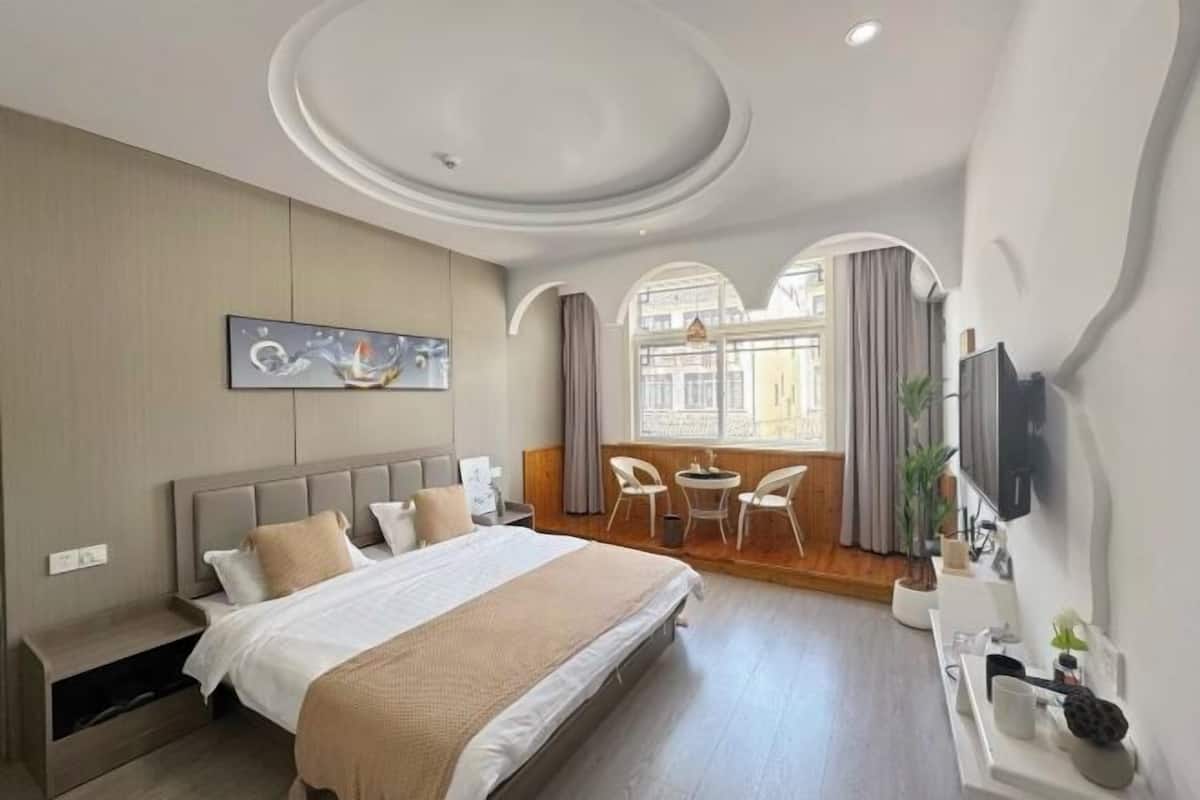 A modern hotel room with a large bed, a dining area, and a TV mounted on the wall.