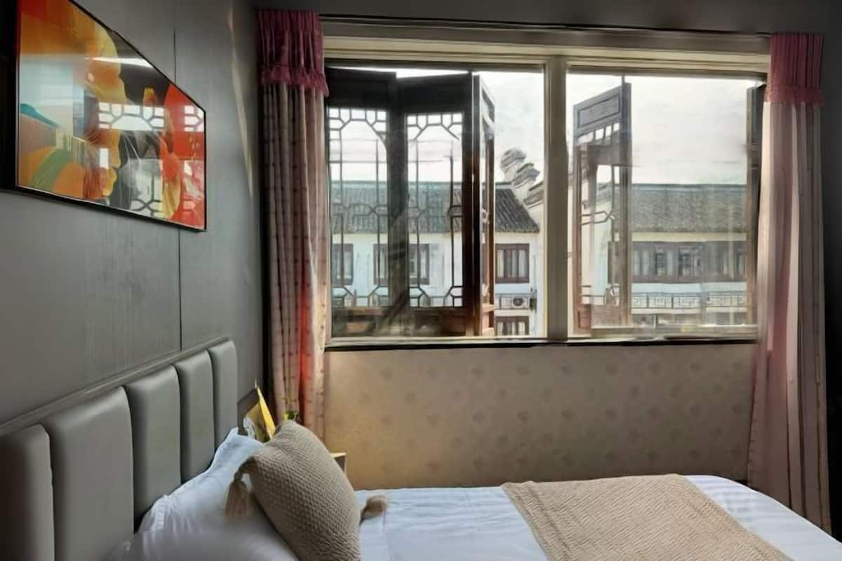 A hotel room with a bed, a window with curtains, and a city view.