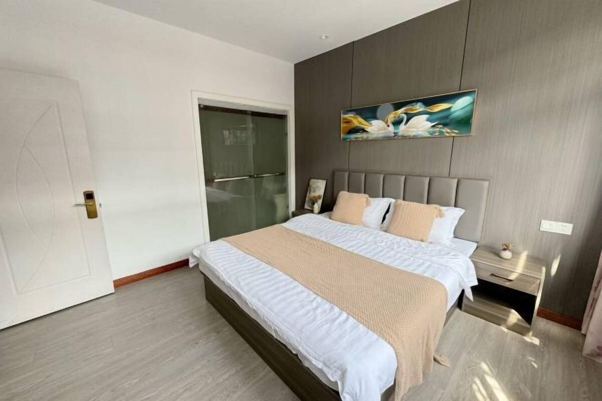A modern bedroom with a large bed, a glass door, and a painting on the wall.