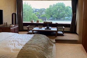 A hotel room with a bed, a dining table with chairs, and a view of a traditional building through the window.