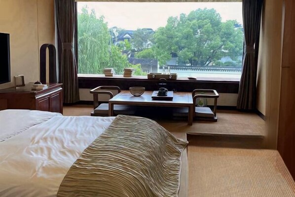 A hotel room with a bed, a dining table with chairs, and a view of a traditional building through the window.