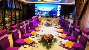 Un salón de conferencias con sillas moradas, una larga mesa con adornos amarillos y un centro de mesa floral.