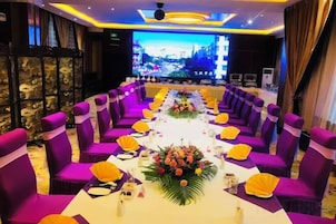 Un salón de conferencias con sillas moradas, una larga mesa con adornos amarillos y un centro de mesa floral.