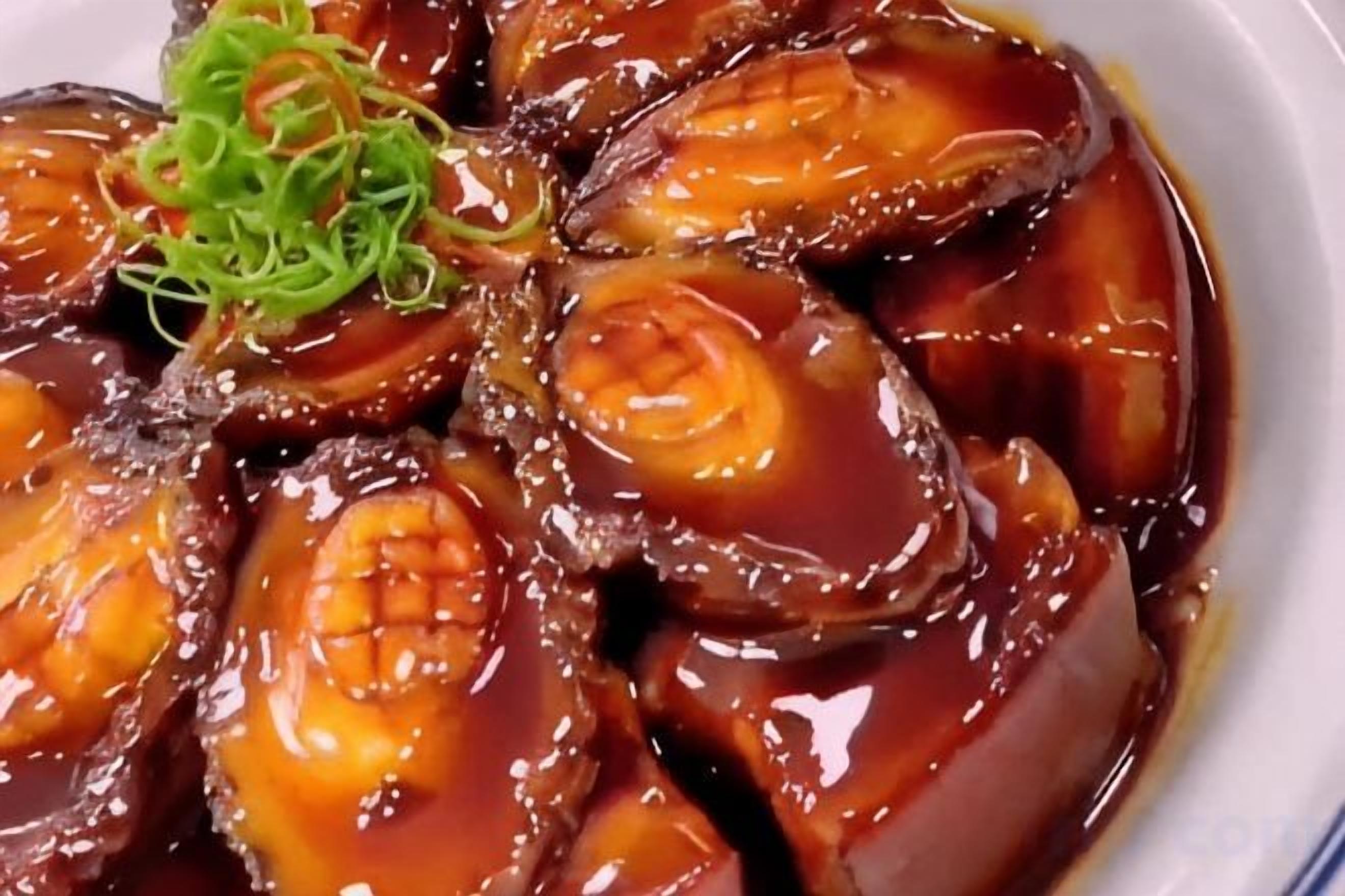 Un plat composé d’aubergines coupées en tranches, glacées et garnies d’oignons verts.