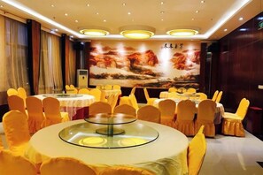 Un salón de banquetes con mesas redondas, sillas amarillas y un amplio mural en la pared.