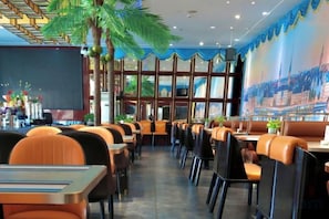 A restaurant with booths and tables, a large mural on the wall, and a palm tree decoration.