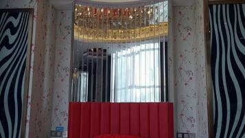 A bedroom with a large mirror, a red headboard, and patterned wallpaper.