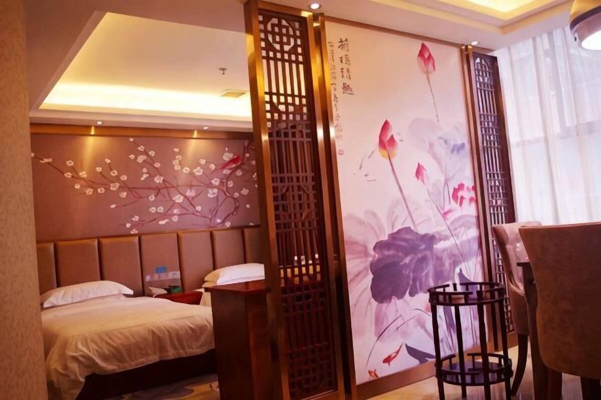 Ein Hotelzimmer mit einem Bett, einem Schreibtisch, einem Sessel, einem dekorativen Raumteiler und einer Wand mit floralen Bildern.