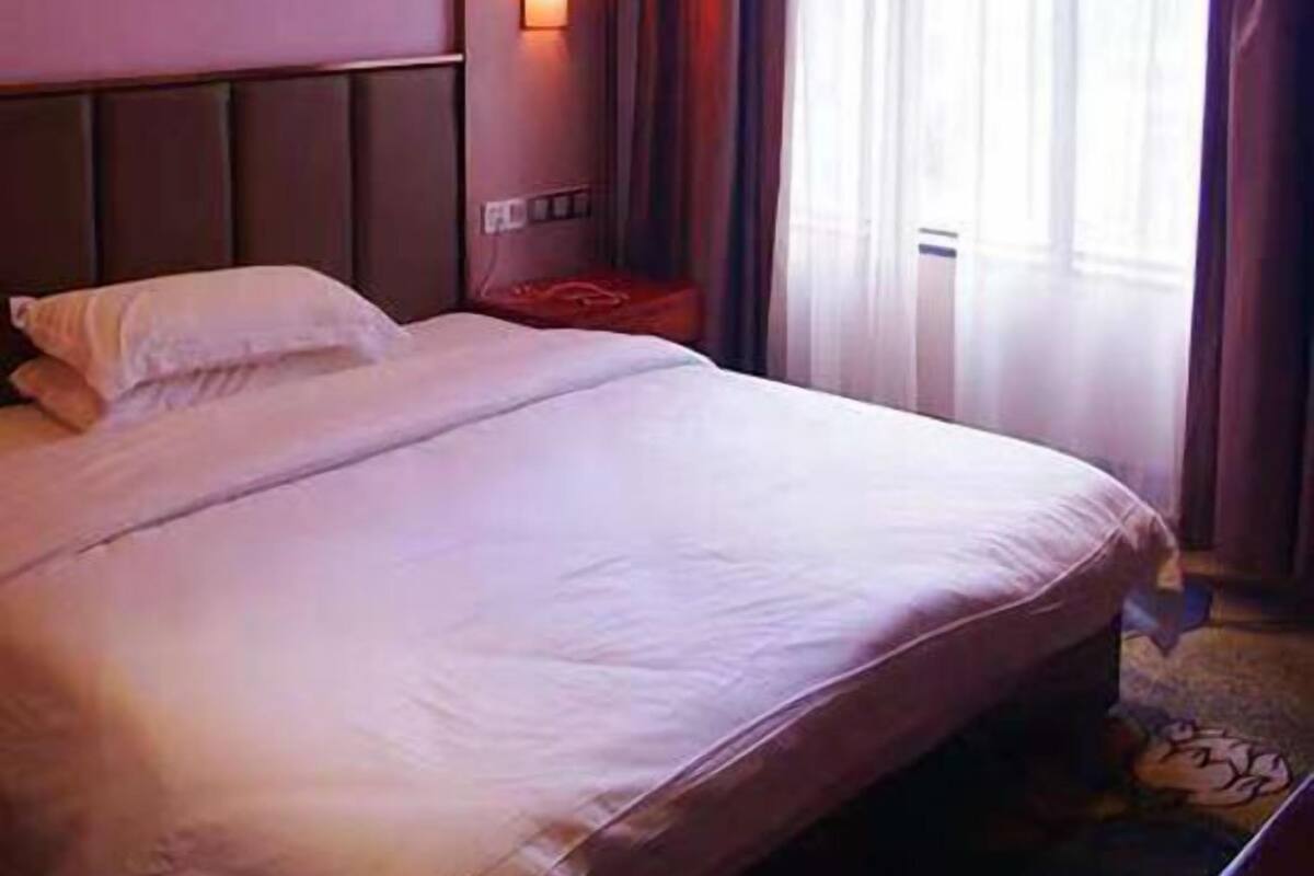 Ein Hotelzimmer mit einem großen Bett, einer Wandleuchte und einem Vorhangfenster.