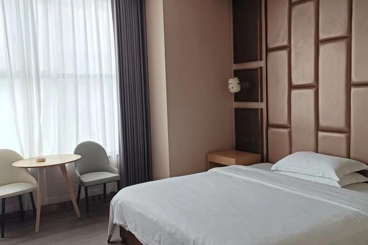 A hotel room with a bed, a small table, two chairs, a nightstand, and a window with curtains.