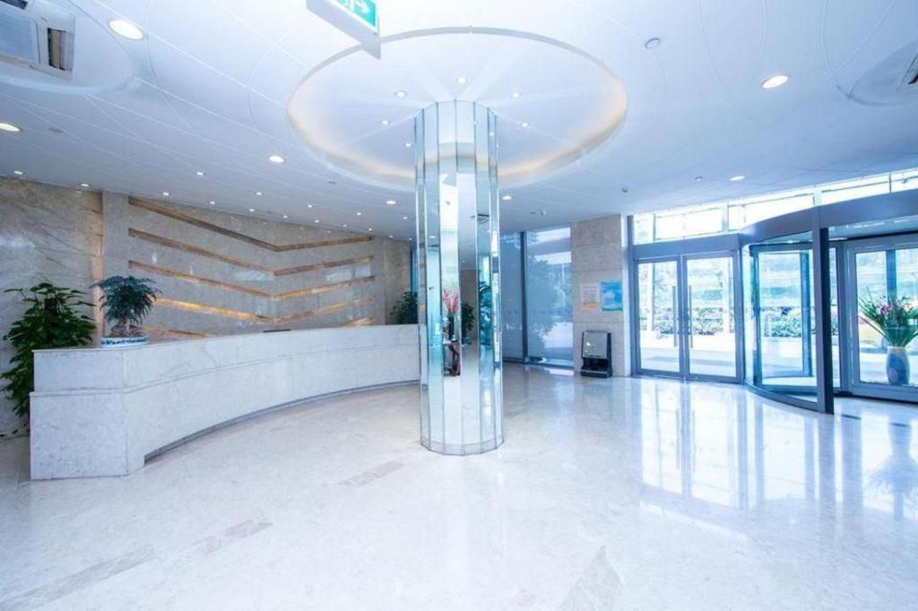 A modern lobby with a central glass column, a reception desk, and large windows.