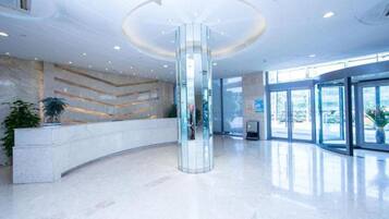 A modern lobby with a central glass column, a reception desk, and large windows.
