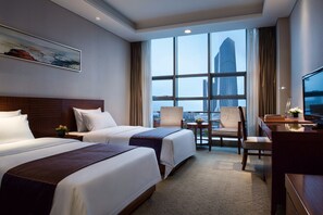 A hotel room with two beds, a desk, a chair, and a large window with a city view.